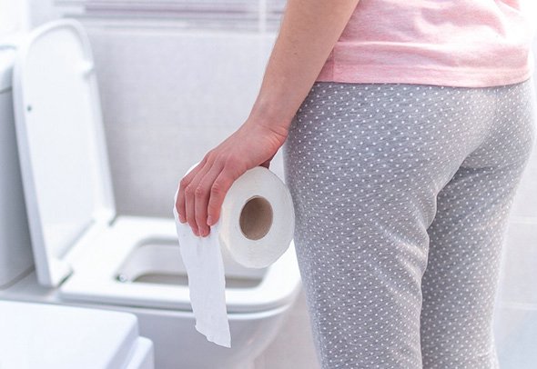 Женщина с туалетной бумагой возле унитаза